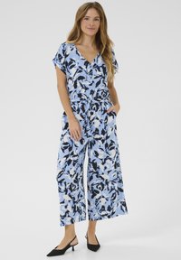 Jumpsuit blu con motivo floreale, maniche corte e pantaloni larghi, dotato di cintura in vita e tasche laterali. Tacchi slingback neri.