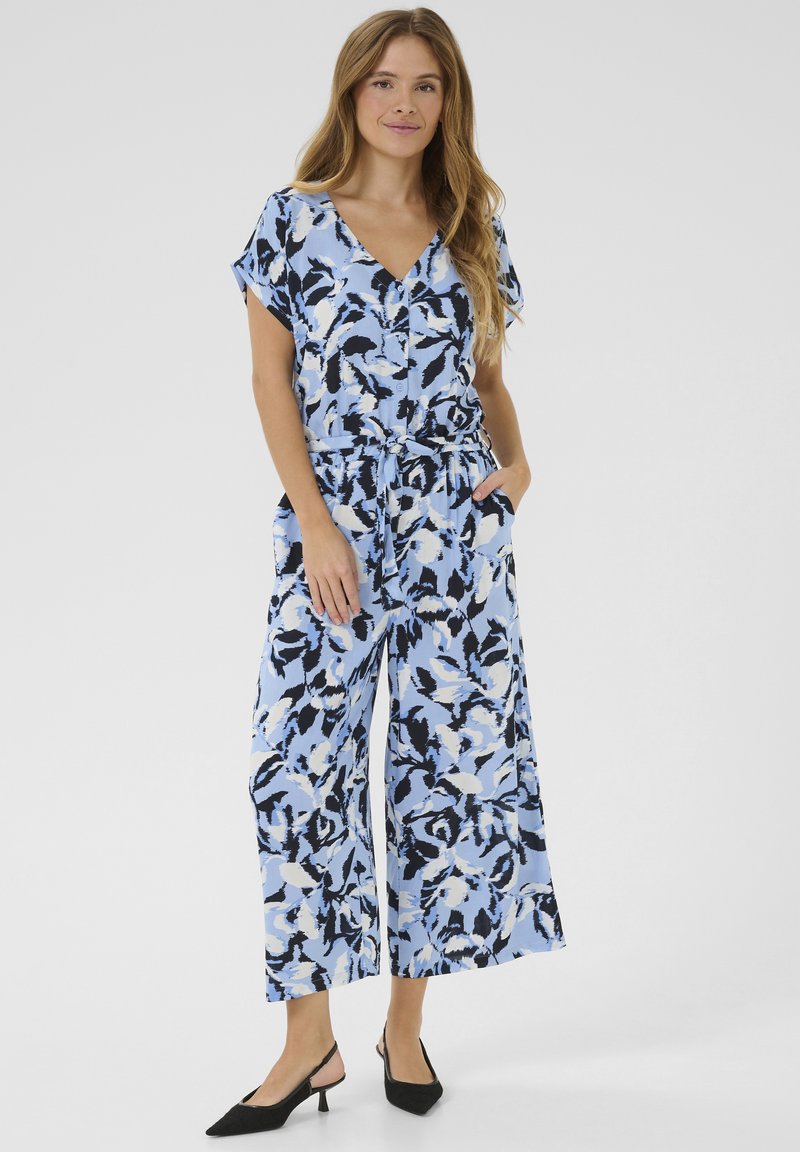 Jumpsuit blu con motivo floreale, maniche corte e pantaloni larghi, dotato di cintura in vita e tasche laterali. Tacchi slingback neri.