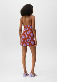 Rotes Kleid mit lila Blumenmuster, Spaghetti-Träger, figurbetonte Silhouette, knielange Länge, glattes Material, kombiniert mit lila Blockabsatzsandalen.