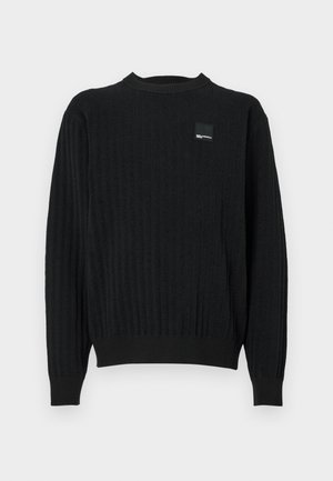 Schwarzer, gerippter Pullover mit Rundhalsausschnitt, der mit strukturiertem Material und einem kleinen Logo-Patch auf der oberen linken Seite versehen ist. Schlichtes und figurbetontes Design.