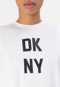 Fehér pamut póló, az elején feltűnő fekete betűk "DK NY" felirattal. Kerek nyakú fazon. Simább textúra, rövid ujjal.