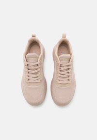 Ljust beige sportskor med mesh-övre, snörningsdesign och vadderad krage. Har texturerade mönster på sidorna och gummisula.