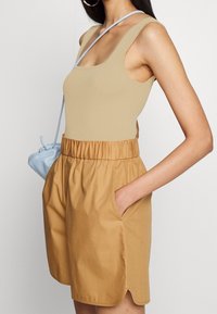 Beige ribbad linne i kombination med bruna högmidjade shorts med elastisk midja och sidfickor; ljusblå väska.