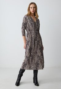 Kleid in Leopard-Print mit Wickeldesign, Dreiviertelärmeln und gerafftem Taillenbereich. Kombiniert mit kniehohen schwarzen Stiefeln.