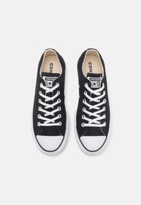 Černé plátěné tenisky s bílými gumovými špičkami a podrážkami. Mají bílé tkaničky a logo na jazyku. Klasický nízký střih.