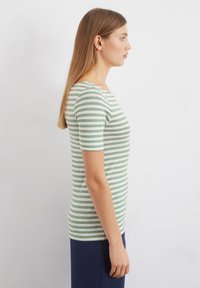 Grün-weiß gestreiftes T-Shirt mit kurzen Ärmeln, taillierter Passform, rundem Halsausschnitt und weichem Stoff. Getragen mit dunkelblauen Hosen.