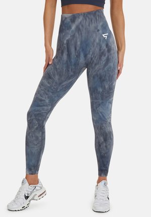 Legíny s vysokým pasem v modro-šedém tie-dye vzoru, vyrobené z elastického materiálu s hladkým povrchem. Obsahují malé bílé logo.