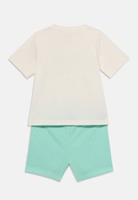 Camiseta de manga corta color crema claro con cuello redondo combinada con pantalones cortos turquesa. Ambos están hechos de una suave y ligera tela de algodón.