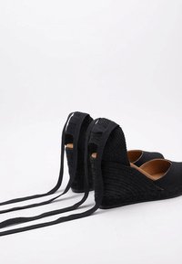 Zapatos de cuña negros con textura trenzada, diseño de punta abierta y lazos ajustables. Presenta una plantilla de color natural y un talón de cuña trenzado.