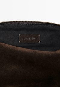 Wnętrze brązowej torebki z zamszu z czarną podszewką; posiada skórzaną metkę wytłoczoną z napisem "Massimo Dutti." Zamek błyskawiczny.