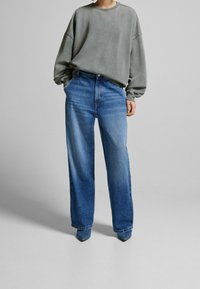 Sweat-shirt gris surdimensionné avec encolure côtelée, associé à un jean bleu clair taille haute à jambes larges et des chaussures bleues pointues à la cheville.