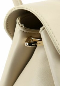 Bolso de mano de cuero beige con una textura suave, con un broche de metal color dorado grabado con "Valentino." Bordes redondeados y diseño minimalista.