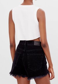 Un haut débardeur côtelé blanc associé à un short en denim noir avec un ourlet effiloché, des poches arrière et une petite étiquette à la taille.