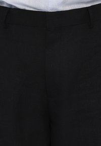 Schwarze Leinenhosen mit glatter Textur, taillierter Passform, Gürtelschlaufen und zwei Seitentaschen. Der Stoff hat ein dezentes Gewebemuster.