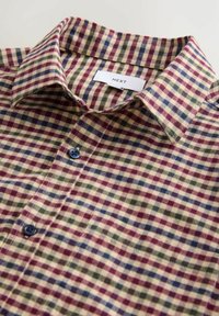 Collared button-up shirt with multicolor check pattern in beige, red, green, and blue, featuring a visible brand label "NEXT" inside collar.