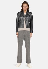 Czarna motocyklowa kurtka z eko-skóry ze srebrnymi elementami, nałożona na beżowy top i wzorzyste, czarno-białe spodnie. Biały sneakersy dopełniają strój.