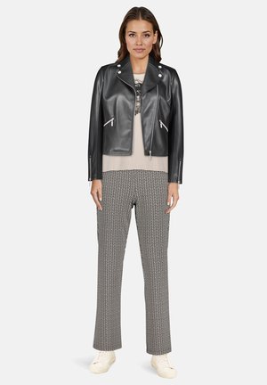 Sort bikerjakke i imiteret læder med sølvfarvet hardware, lagdelt over en beige top og mønstrede sorte og hvide bukser. Hvide sneakers fuldender outfittet.