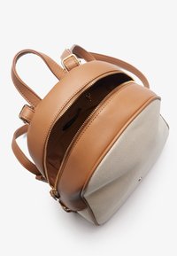 Mochila de cuero marrón con un fondo texturizado beige, aberturas con doble cremallera y correas ajustables. Presenta acentos de hardware en tono dorado.