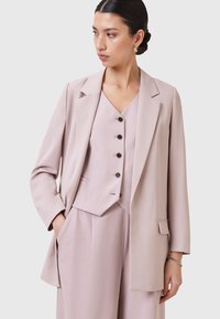 Blazer rosa chiaro con una vestibilità su misura, revers classici, chiusura con un solo pulsante e tasche laterali, abbinato a un gilet coordinato con dettagli a bottoni.