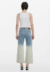 Weite Jeans aus hellblauem Denim mit einem sanften Farbverlauf zu blassem Grün. Die Rückansicht zeigt zwei aufgesetzte Taschen und ein braunes Lederetikett.