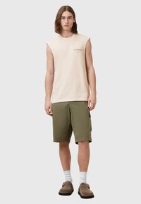 Ermeløs lyserosa skjorte med logo, kombinert med olivengrønne cargoshorts. Brukt med hvite sokker og brune slip-on sko.