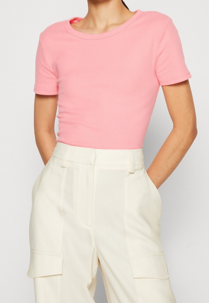 Maglietta rosa a coste a maniche corte con scollo tondo, abbinata a pantaloni crema a vita alta con tasche laterali e una texture liscia.