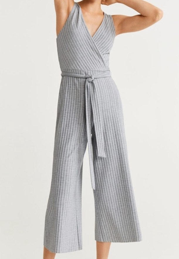 Femme portant une combinaison grise sans manches côtelée avec jambes larges et ceinture nouée à la taille, debout les bras levés derrière la tête.