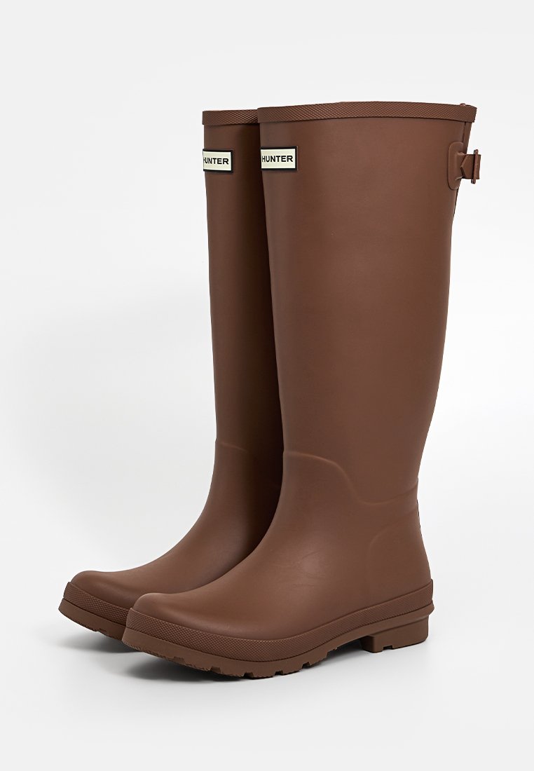 Braune Gummiregenstiefel mit glatter Oberfläche, runder Zehenpartie und einer robusten Sohle. Merkmale sind ein verstellbarer Riemen und Logotags an der Vorderseite.
