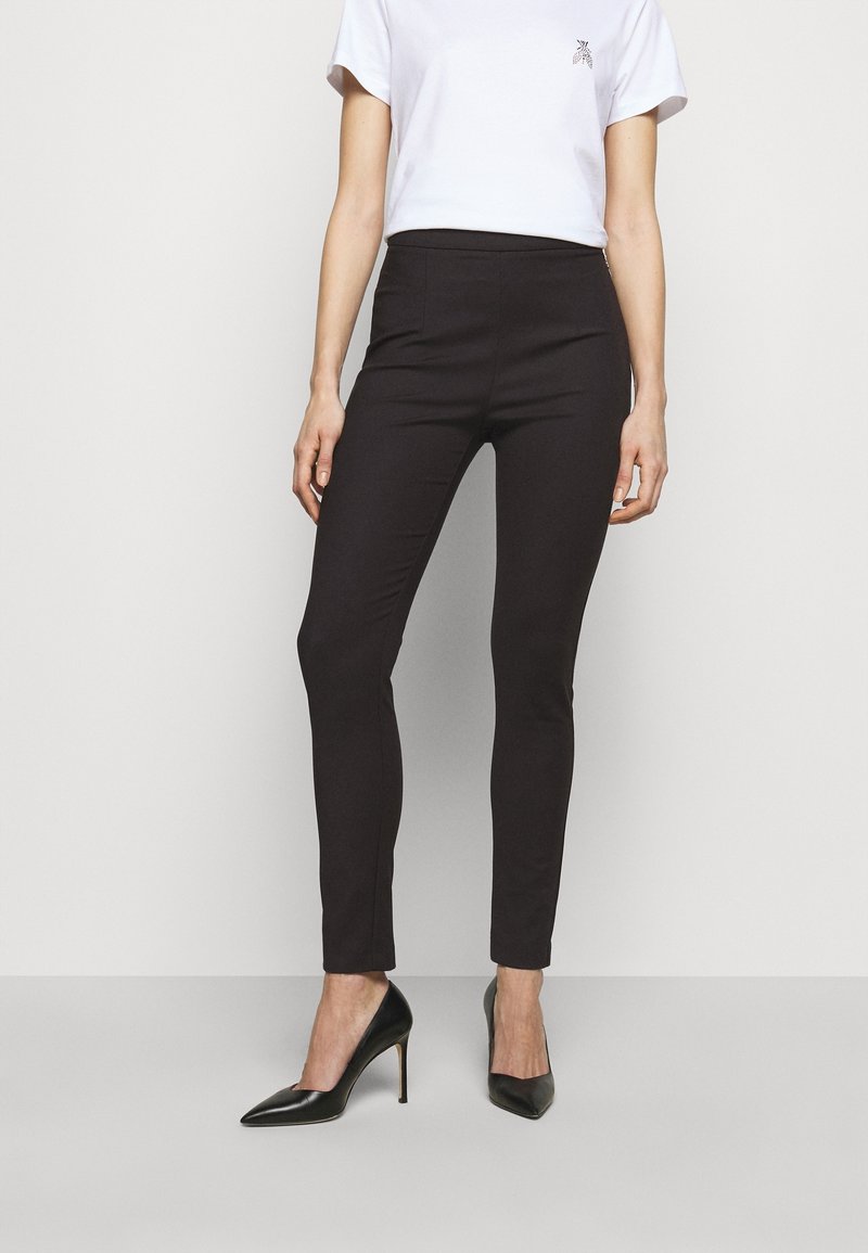 Schwarze, taillierte Hosen mit glatter Textur, hoher Taille und Knöchellänge. Kombiniert mit einem einfachen weißen T-Shirt und schwarzen High Heels.