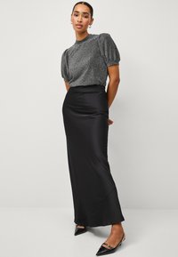 Zwarte satijnen maxi rok met een gladde textuur, gecombineerd met een aansluitend, glinsterend grijs topje met korte mouwen en pofmouwen.