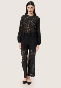 Tutt'uno in pizzo nero con maniche lunghe, design peplum e sezioni trasparenti. Texture liscia con intricati motivi floreali.