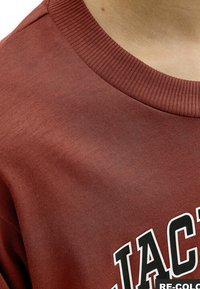 Sweat-shirt bordeaux avec un col côtelé, présentant un motif imprimé blanc. Texture de tissu douce avec une coupe décontractée et relaxante.