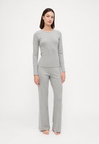 Haut à manches longues gris et pantalon assorti en matériau tricoté. Le haut présente un col rond ; le pantalon a une coupe décontractée et des jambes droites.
