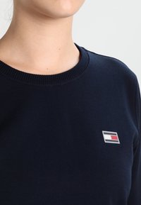 Felpa in cotone blu navy con collo a girocollo a costine e un piccolo logo ricamato in rosso, bianco e blu sul petto.