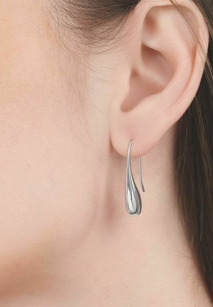 Zilveren druppelvormige oorbel die hangt aan een doorgestoken oor, met stijl bruin haar zichtbaar achter het oor.