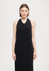 Svart halterneck kjole med en tettsittende bodice og svømmed kjole, laget av mykt materiale. Minimalistisk design uten synlige mønstre eller aksenter.