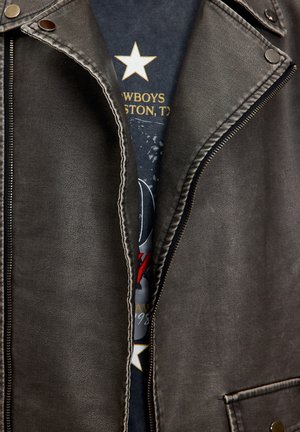 Black leather jacket with silver hardware, featuring a visible zipper and contrasting white stitching, reveals a dark graphic t-shirt underneath.