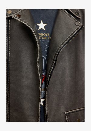 Zwarte leren jas met zilverkleurige accenten, met een zichtbare rits en contrasterende witte stiksels, waardoor een donker grafisch T-shirt eronder zichtbaar is.