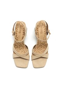 Beige mokkasandaalit, joissa on korkea korko, ristikkäiset hihnat ja säädettävä nilkkahihna. Teksturoitu sisäpohja, jossa on lehtikuvio. Neliönmuotoinen varvasdesign.