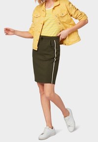 Sukně olivové barvy s bílým bočním pruhem, spárovaná se žlutou džínovou bundou a žlutým pruhovaným tričkem. Bělé sneakers dokončují outfit.