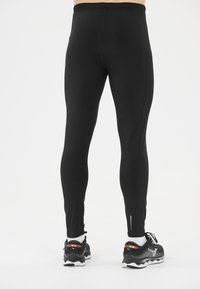 Schwarze sportliche Leggings mit glatter Textur, ausgestattet mit einem hohen Taillenbund und Akzentnähten, kombiniert mit schwarz-weißen Sneakers.