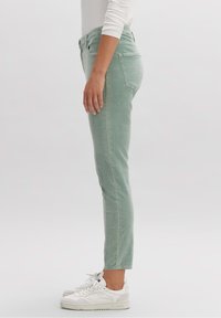 Pantalones ajustados de color verde claro, elaborados con una tela suave, con una cintura de altura media, bolsillos laterales y traseros, combinados con zapatillas blancas.