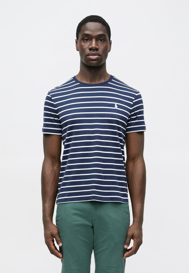 Tumši zila svītraina T-krekls ar baltām horizontālām svītrām un nelielu logotipu uz krūtīm; apaļa apkakle, īsas piedurknes, kokvilnas materiāls.