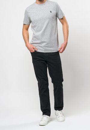 T-shirt grigia in cotone con scollatura rotonda e piccolo logo navy, abbinata a pantaloni neri e sneaker bianche. Vestibilità casual e design semplice.