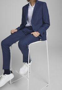 Námořnický modrý oblek se strukturovaným povrchem, s jedním knoflíkem na saku a přiléhavými kalhotami, doplněný bílými teniskami.