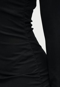 Μαύρο ριμπ φόρεμα με εφαρμοστή σιλουέτα και ρυτίδωση στη μία πλευρά. Η υφή είναι λεία και ελαφρώς ελαστική.