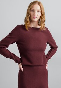 Burgunderfarbener Strickpullover mit langen Ärmeln und rundem Halsausschnitt, kombiniert mit einem passenden Rock; weiche Textur und schlichtes Design.
