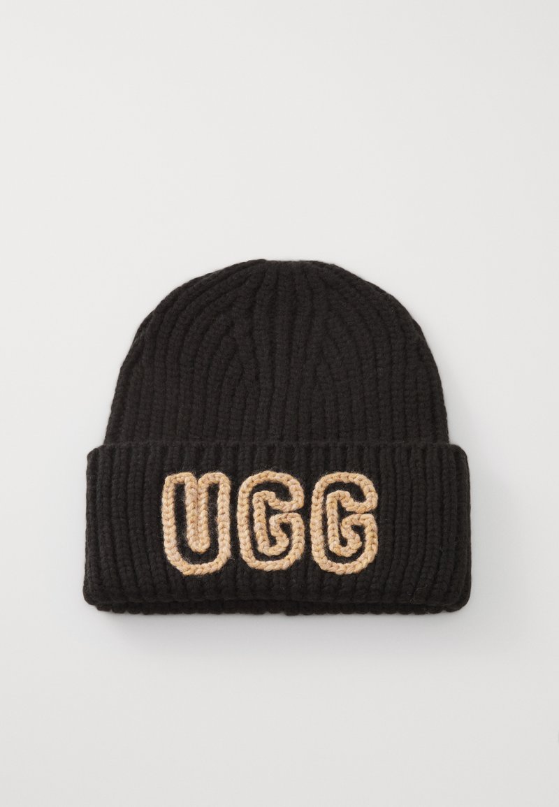 Czarna dzianinowa czapka w stylu beanie z żebrowaną fakturą i złożonym mankietem, na którym widnieje wyraźny beżowy napis "UGG". Wygląda na ciepłą i elastyczną.