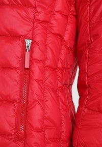 Červená prošívaná pufrová bunda se zipovou kapsou. Hladká, lesklá tkanina s texturovaným, polstrovaným designem. Kovové akcenty na zipu v stříbrné barvě.