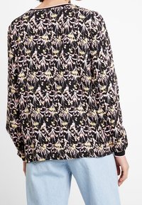 Blusa a maniche lunghe in tessuto nero con motivo floreale in rosa e giallo. Presenta un collo rotondo e polsini elasticizzati, vestibilità comoda.